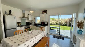 Una cucina moderna con zona pranzo, frigorifero, forno a microonde e vista su un giardino tramite una porta finestra.