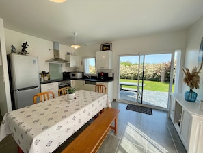 A modern kitchen with a dining area, a refrigerator, microwave, and a view of a garden through a sliding glass door. - Recent house in quiet area - 4 guests (Bretignolles-sur-Mer)