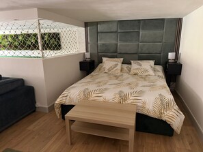 Ein Schlafzimmer mit einem Bett, Nachttischen, einer Bank, einem Fenster mit Blick ins Grüne und einem Kopfteil.