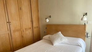 Een bed met een houten hoofdbord, een wit kussen en een wandlamp.