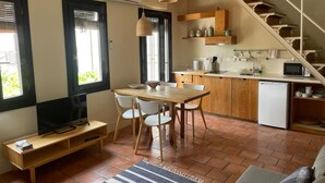 Een ruimtelijk ingerichte leefruimte met een eethoek, kitchenette en een trap.