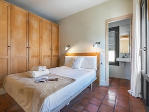 Ein Schlafzimmer mit einem Bett, einem Holzschrank, einer Nachttischlampe und einem durch eine offene Tür einsehbaren Badezimmer.