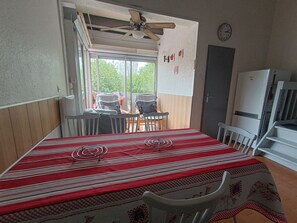 Ein Essbereich mit Tisch, der mit einer gestreiften Tischdecke bedeckt ist, Stühlen, einem Deckenventilator und Blick durch ein Fenster.