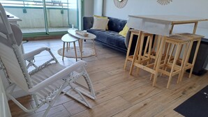A room with a convertible chair, a small round table, a sofa with cushions, and a wooden table with chairs. - Apartment sea view - 4 guests (Fort-Mahon-Plage)