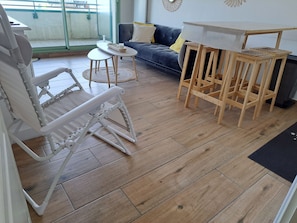 A room with a convertible chair, a small round table, a sofa with cushions, and a wooden table with chairs. - Apartment sea view - 4 guests (Fort-Mahon-Plage)