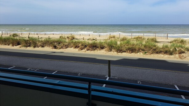 A beach view with a fence, grassy dunes, and a road in the foreground. - Apartment sea view - 4 guests (Fort-Mahon-Plage)