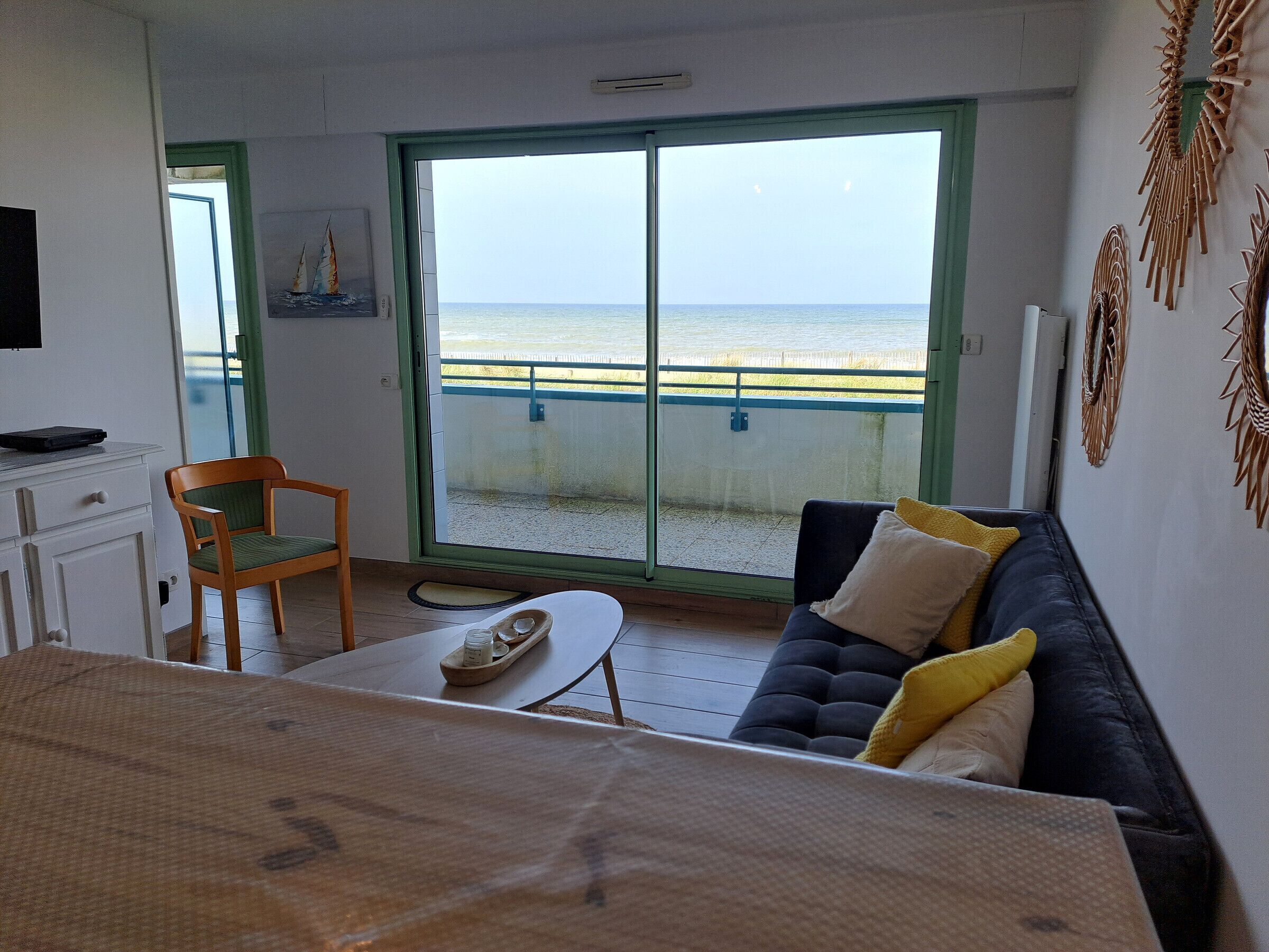 Ein Zimmer mit einer Sitzecke, einem Sessel, einem Tisch, einem Fernseher und Meerblick durch eine Schiebetür.