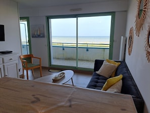 A room with a sofa, a chair, a table, a TV, and a view of the sea through a sliding door. - Apartment sea view - 4 guests (Fort-Mahon-Plage)