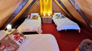 Un dormitorio acogedor en el ático con dos camas, alfombra roja, vigas de madera y una cortina amarilla.