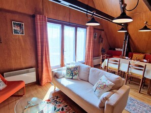 A cozy room with a sofa, a dining table, and a red chair. - Charming chalet, panoramic view - 5 guests (Saint-Michel-de-Chaillol)