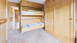 A room with a bunk bed, wooden wardrobe, and a door leading to another room. - Cozy apartment at the slopes with WiFi and parking (Les Gets)