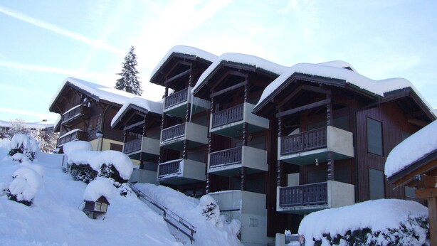 A multi-story hotel with balconies, surrounded by snow-covered trees and a clear sky. - Cozy apartment at the slopes with WiFi and parking (Les Gets)