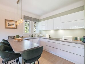 A modern kitchen with white cabinets, a dining table with chairs, a pendant light, and a window with curtains. - Ideal apartment, pets allowed, city centre (Le Touquet-Paris-Plage)