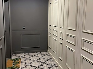 A narrow hallway with grey walls, a patterned floor, and a door with a small label.
