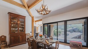 A dining area with a wooden table set for four, surrounded by chairs, a large wooden cabinet with glass doors, and a chandelier. - Spacious penthouse with mountain view - 8 guests (Argentière)