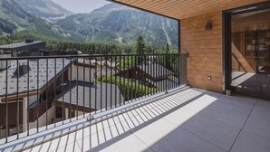 A balcony with a view of mountains, a wooden ceiling, and a glass door leading to a room with bookshelves. - Spacious penthouse with mountain view - 8 guests (Argentière)