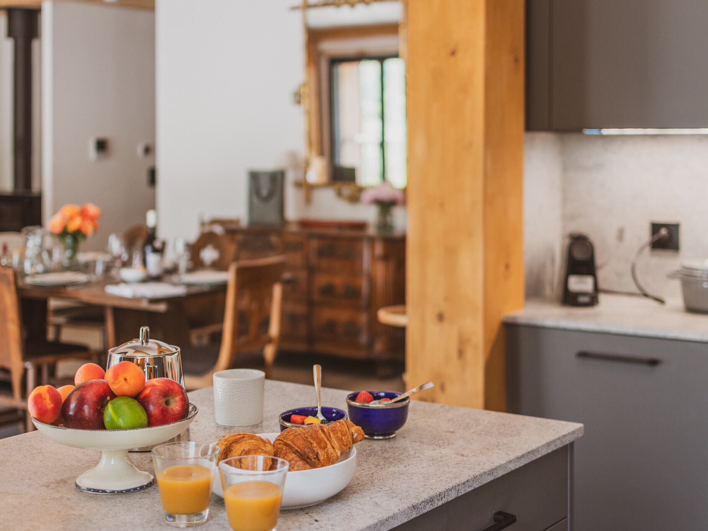 Ein Frühstückstisch mit Früchten, Croissants und Saft auf einer Küchenarbeitsfläche.
