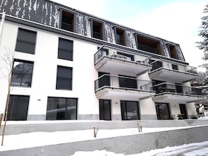 Ein mehrstöckiges Gebäude mit Balkonen, großen Fenstern und einem mit Schnee bedeckten Untergrund.