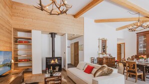 A cozy living room with a fireplace, wooden beams, a sofa, and a dining area. - Spacious penthouse with mountain view - 8 guests (Argentière)