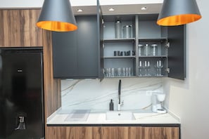 A modern kitchen with a black refrigerator, wooden cabinets, a marble countertop, and two pendant lights.