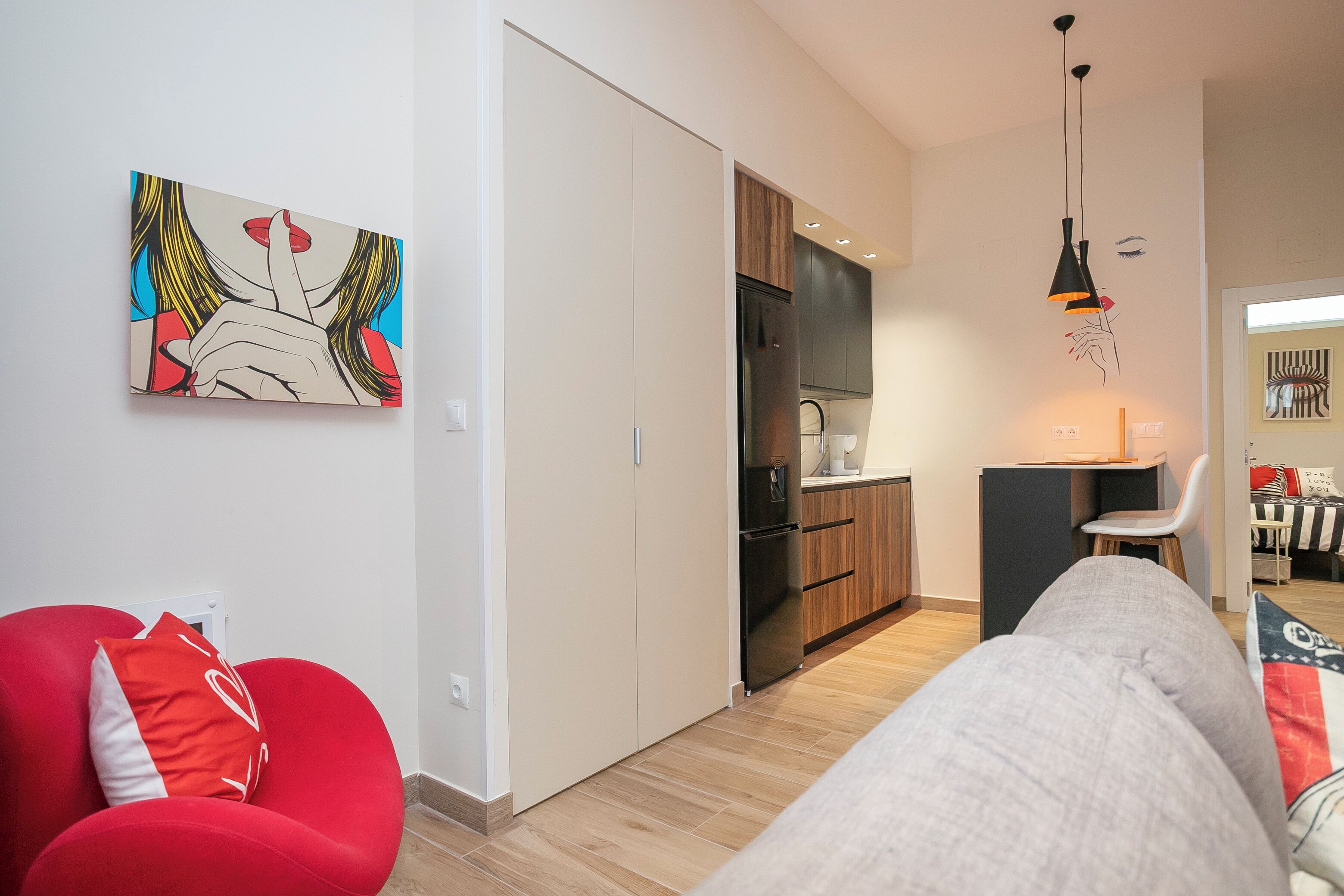A modern apartment with a kitchenette, a dining area, and a living space with a red chair and a sofa.
