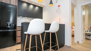 Una cocina moderna con armarios negros, un refrigerador negro y dos taburetes blancos.