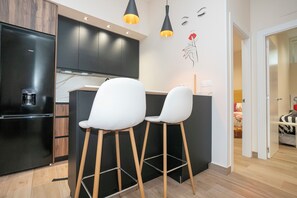 A modern kitchen with black cabinets, a black refrigerator, and two white bar stools.