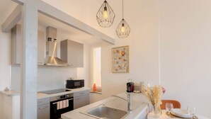 A modern kitchen with a central island, stainless steel appliances, pendant lighting, and a dining area with a table set for two. - Maison Mon Idée | Top floor, Bright, sea view and Palais des Festivals (Cannes)