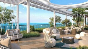 Een moderne buitenlounge met zitplaatsen, een schommelstoel en uitzicht op de oceaan.