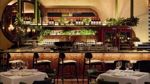 Een bar met een marmeren aanrecht, wijnflessen, glazen en potplanten.