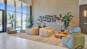 Een ruime lobby met grote ramen, een zithoek met banken en stoelen, en decoratieve wandkunst.