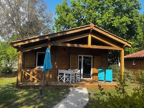 Eine Holzhütte mit einer Veranda, weißen Möbeln und einem blauen Regenschirm.
