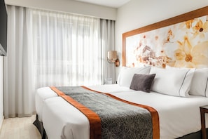 Habitación de hotel con una cama grande, una mesita de noche, una lámpara y una ventana con cortinas translúcidas.