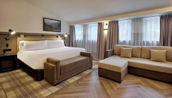 Una habitación de hotel con una cama, un sofá, una mesita de noche, una lámpara y un cuadro en la pared.