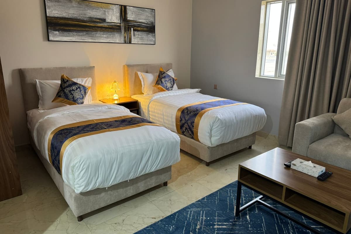 Habitación de hotel con dos camas, un escritorio, una silla, un cuadro en la pared y una ventana con cortinas.
