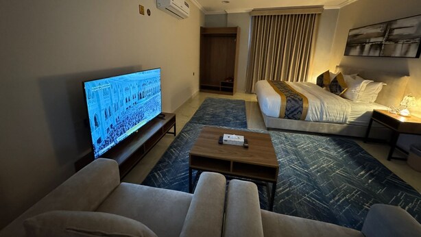 Una habitación de hotel con televisión, sofá, cama, mesita de café y cortina.