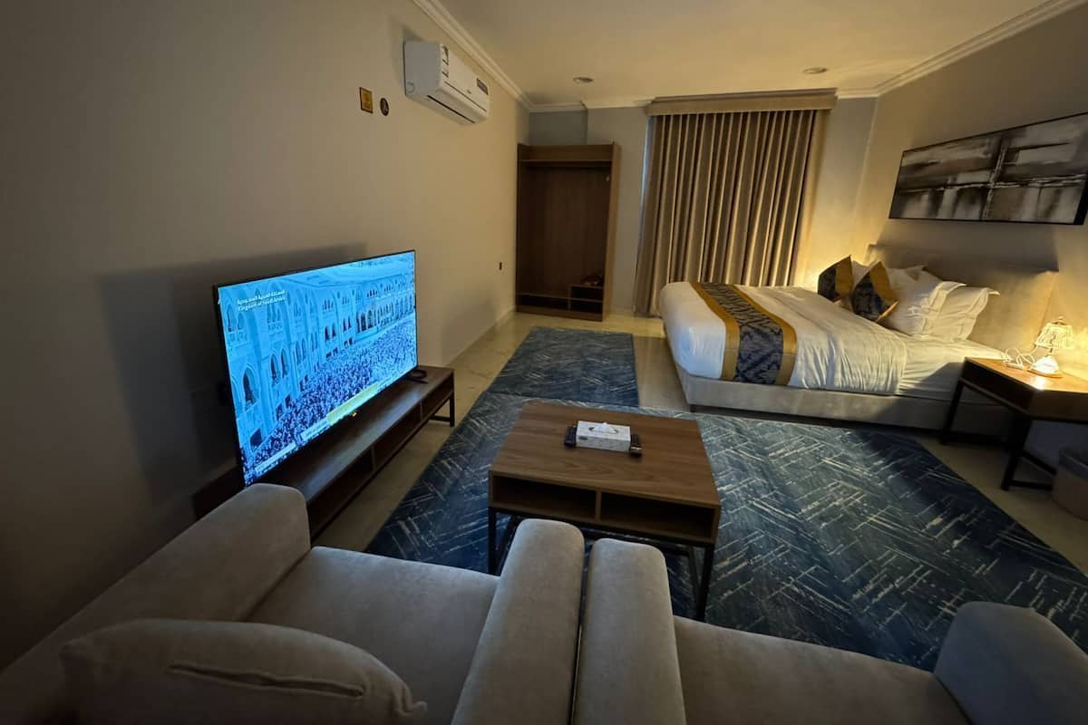 Una habitación de hotel con televisión, sofá, cama, mesita de café y cortina.