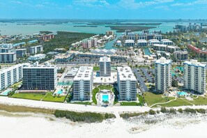 Un complejo turístico en la costa con edificios altos, una piscina central y un puerto deportivo.