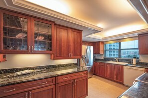Una cocina con armarios de madera, encimeras de granito, electrodomésticos de acero inoxidable y un ventanal con vista a la ciudad.