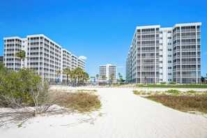 Un hotel frente a la playa con varios edificios altos, un camino de arena y palmeras.