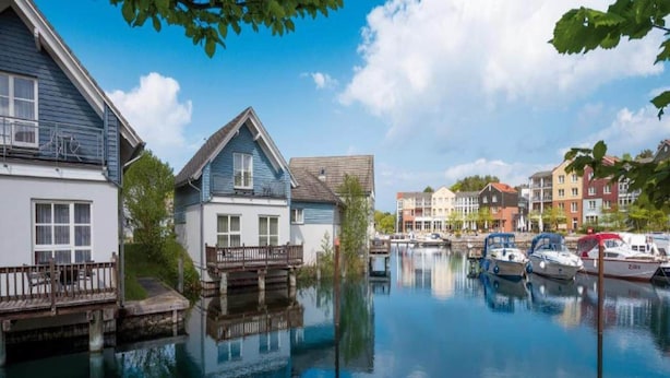 Ein Gebäude am Kanal mit einem Anleger, Booten und weiteren Gebäuden im Hintergrund.