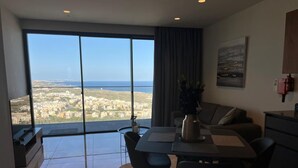 Ein modernes Wohnzimmer mit einem großen Schiebeglasfenster zum Balkon, einem Essbereich mit Tisch und Stühlen, einer Couch und einem Bild an der Wand.