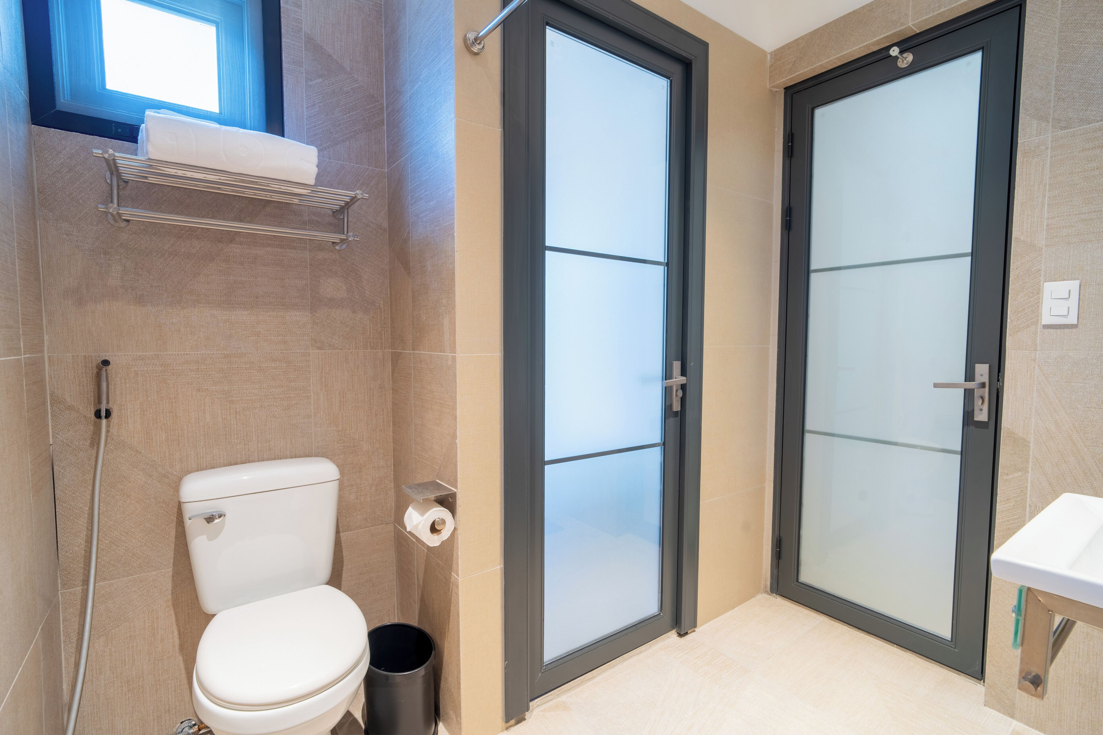 A bathroom with a toilet, a glass shower door, a sink, and a towel rack.