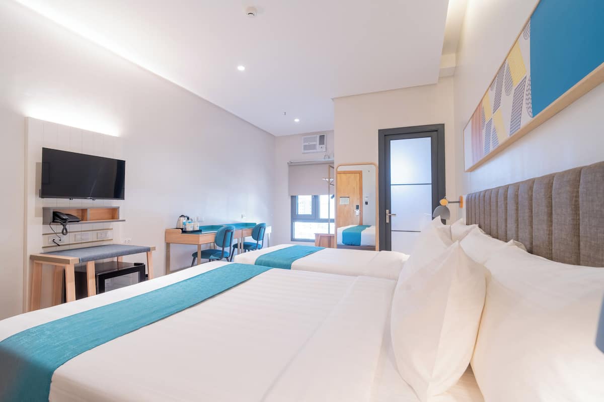 Une chambre d’hôtel avec deux lits, un bureau, une chaise, une télévision et une porte donnant sur une autre pièce.