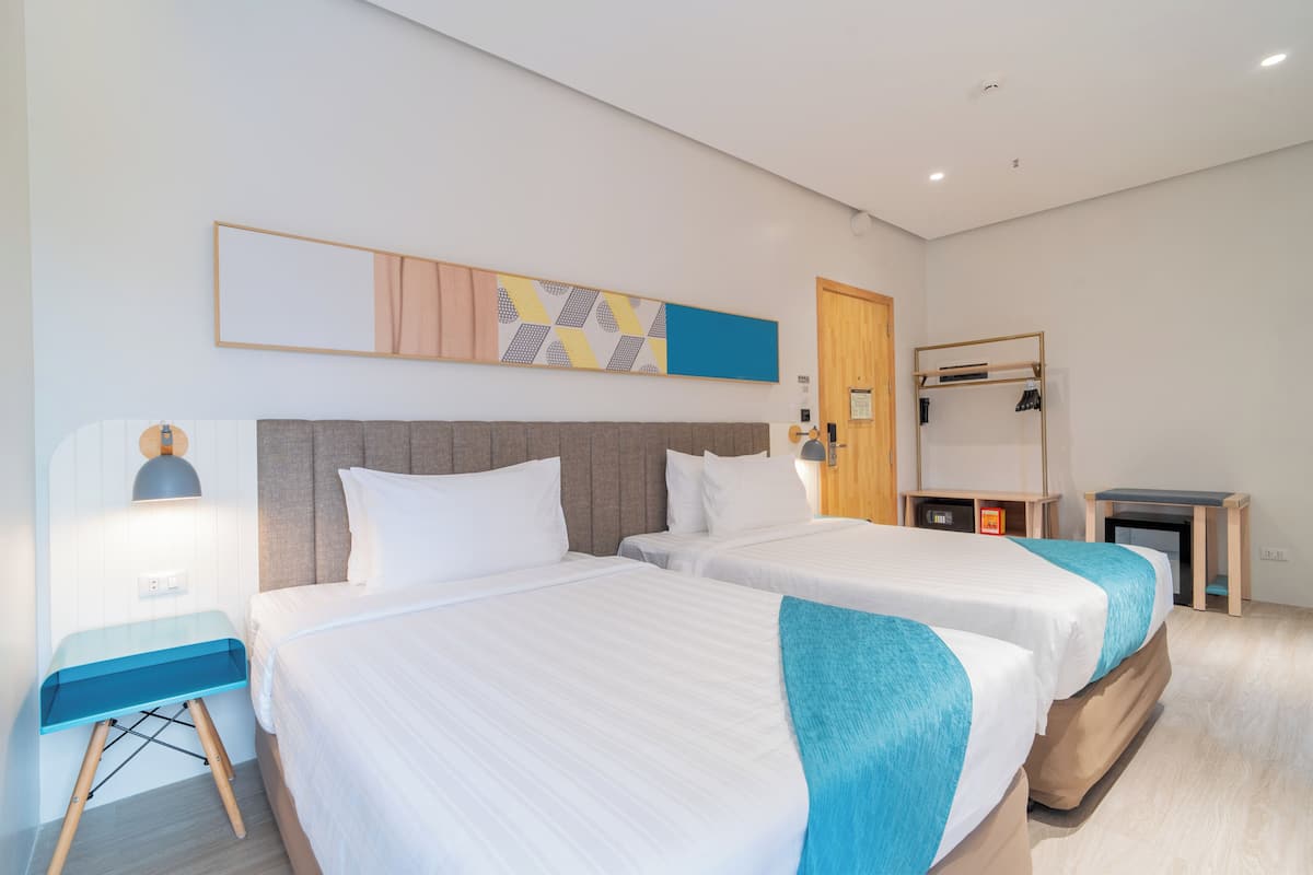 Une chambre d’hôtel avec deux lits, un bureau, un miroir et une œuvre d’art accrochée au mur.
