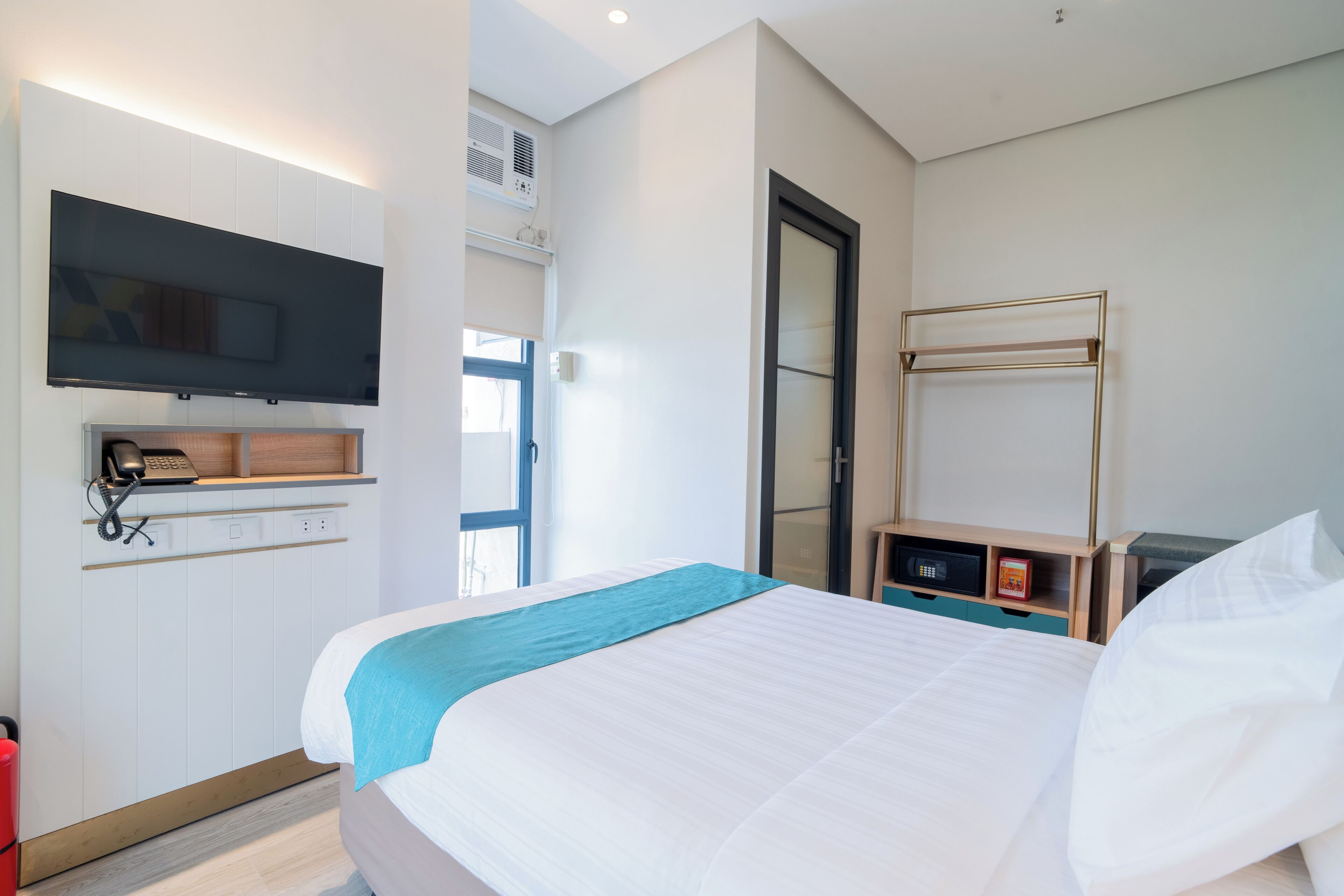 A hotel room with a bed, a TV mounted on the wall, a desk with a phone, and a bunk bed.
