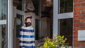A statue of a man in a striped robe outside a building with a metal railing and a potted plant nearby. - HOTEL DÜNENLÄUFER Langeoog (Langeoog)