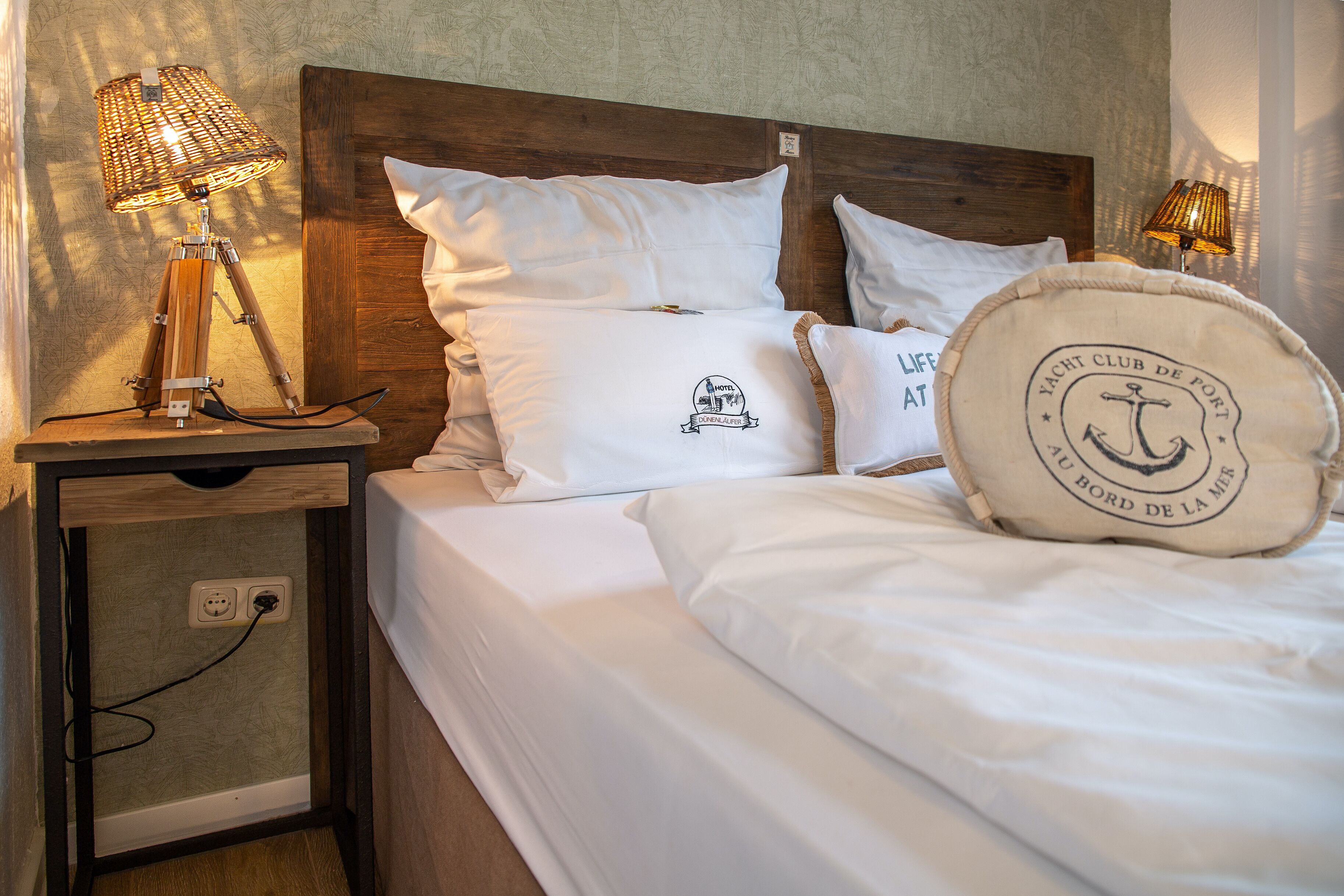 Una cama bien hecha con sábanas blancas, cabecera de madera y dos lámparas de noche.