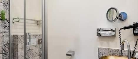 Un baño con cabina de ducha de vidrio, pared con azulejos de mármol, tocador de madera con lavamanos dorado y un inodoro.