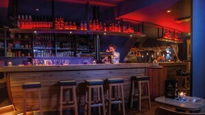 A bar area with wooden stools, shelves of bottles, and a bartender. - HOTEL DÜNENLÄUFER Langeoog (Langeoog)